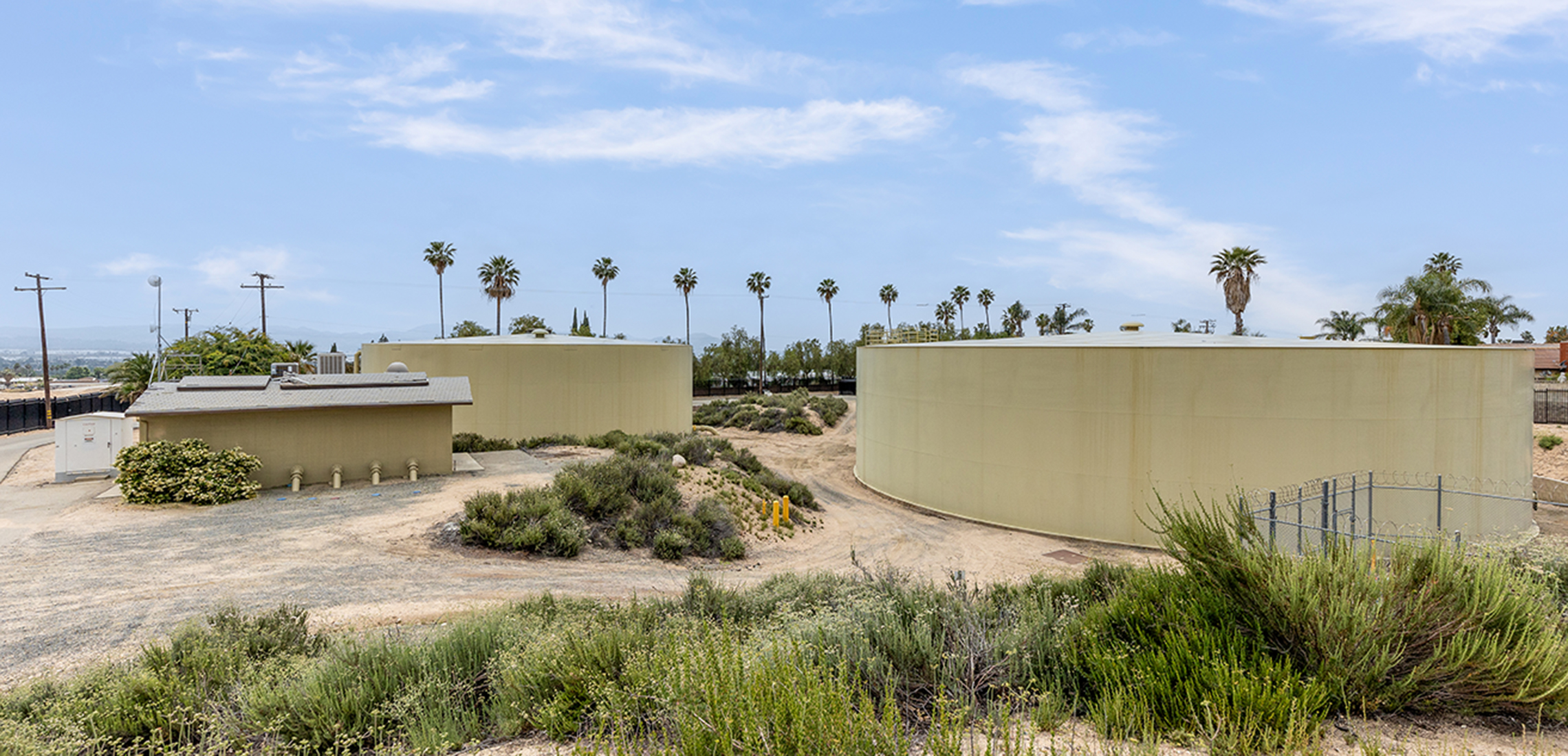 Two reservoirs and a pump station in a dirt lot with grasses