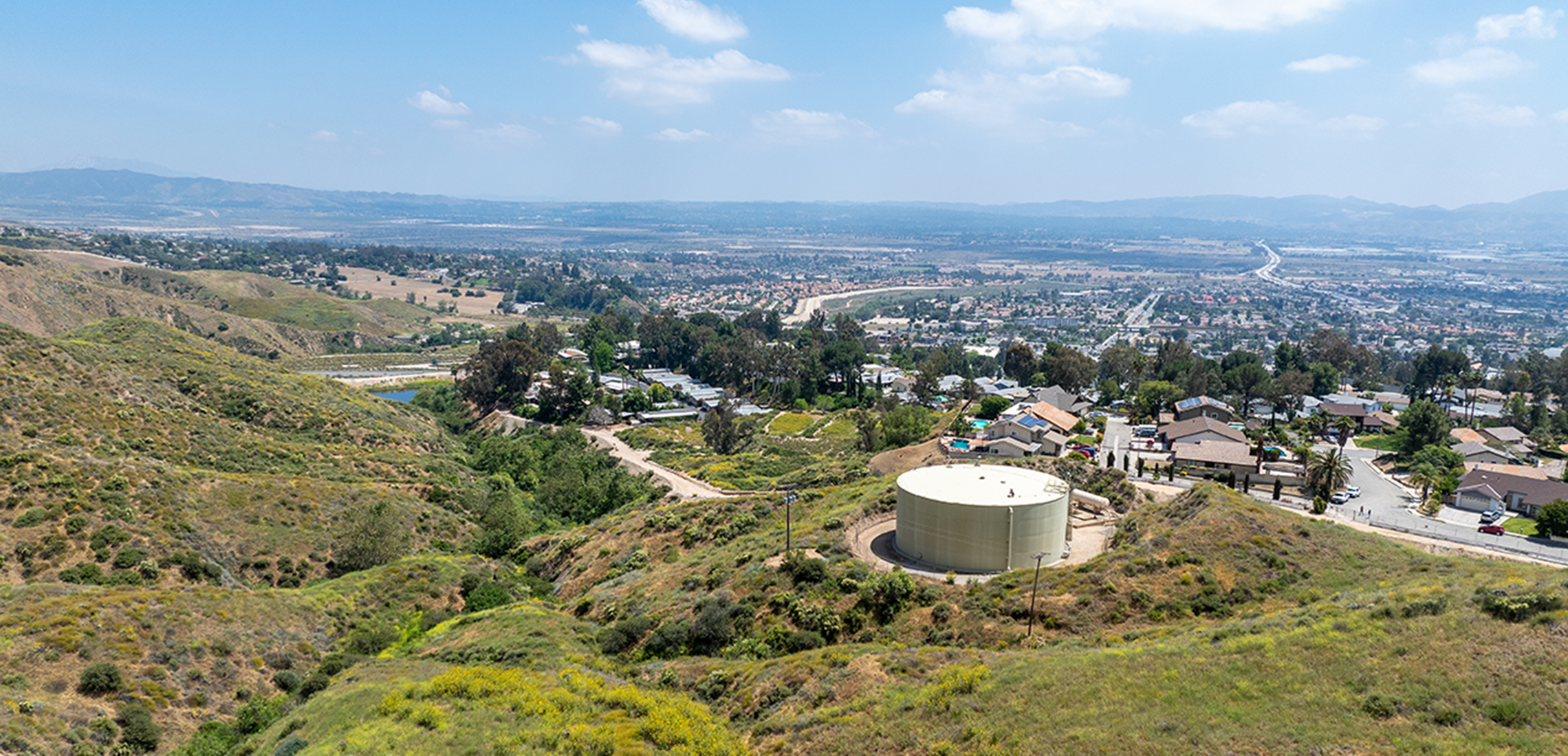 Reservoir on grassy hill overlooking valley with homes. 